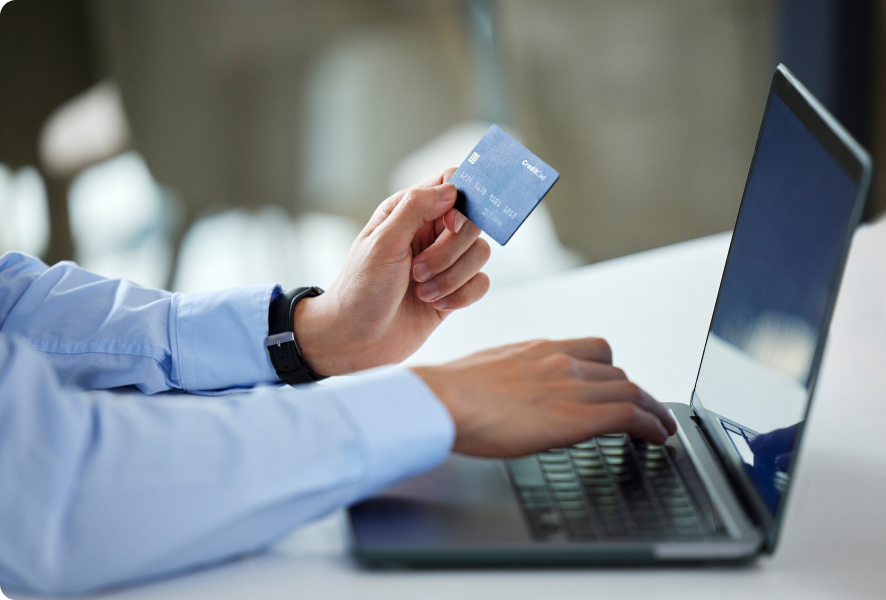 Close-up of a person holding a credit card while using a laptop for online payment