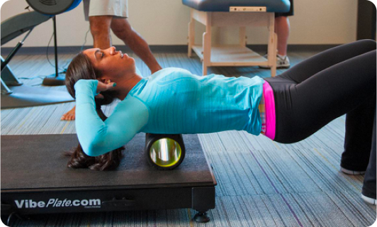 Woman lying on a VibePlate using a foam roller for back exercise