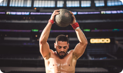 Isaiah Vidal lifting a medicine ball overhead in a stadium, showcasing his athletic prowess as a Spartan Champion and CrossFit Athlete